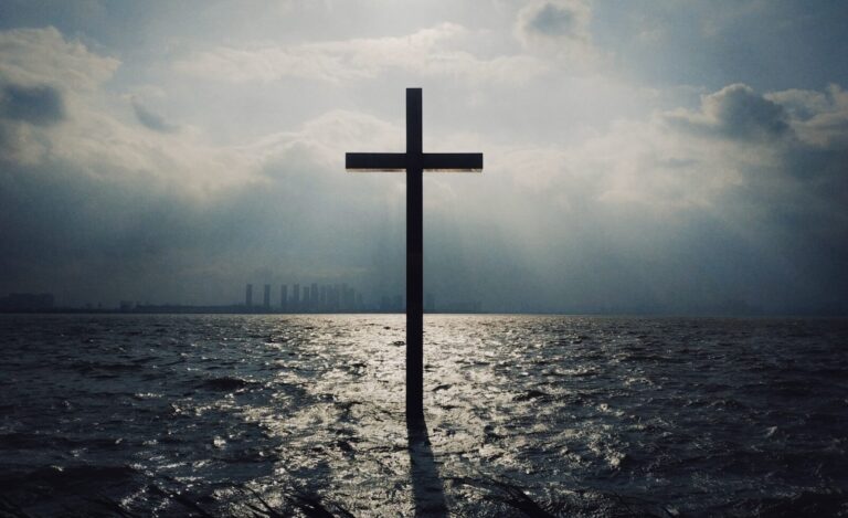 Cross standing in the ocean beneath a cloudy sky