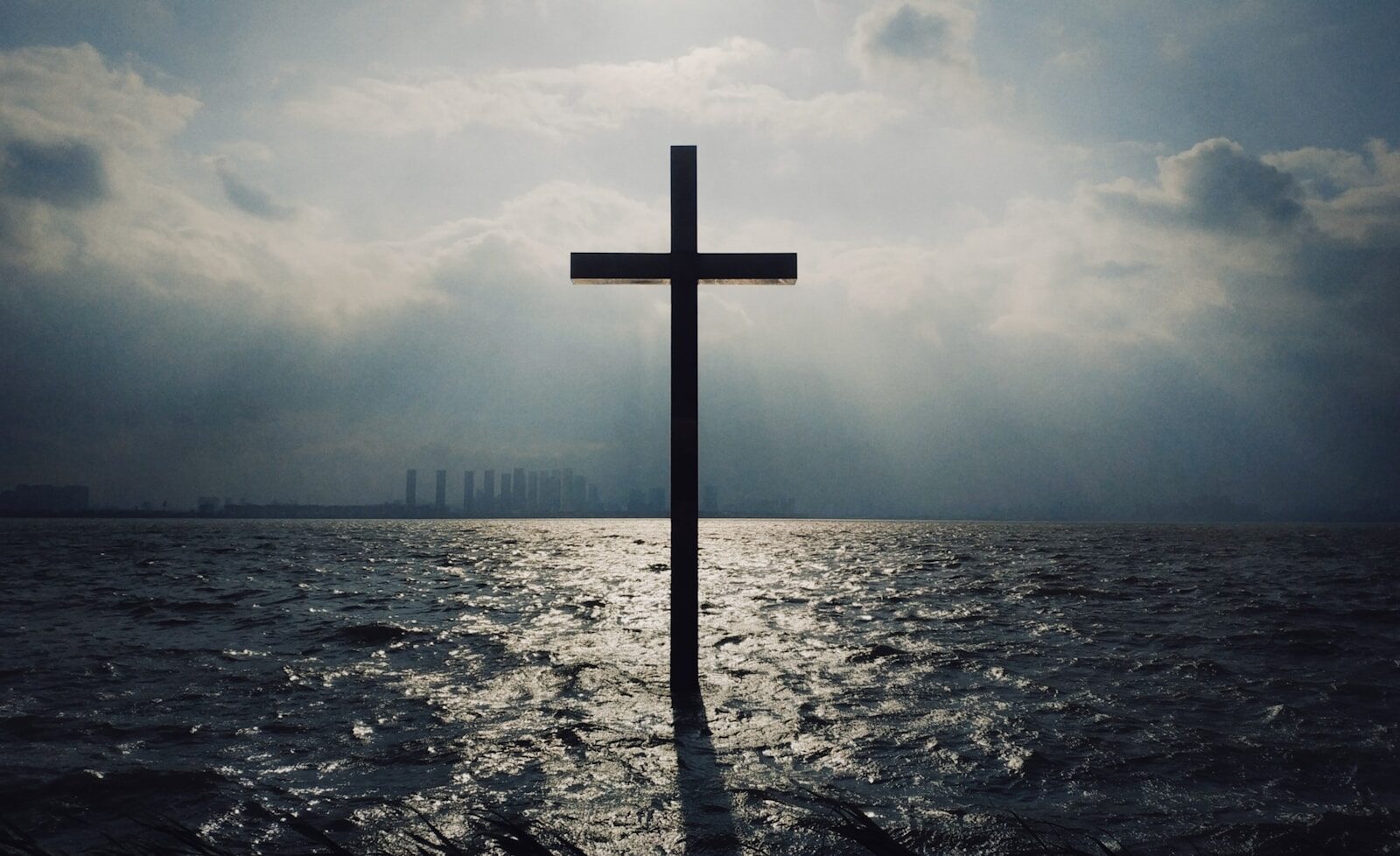 Cross standing in the ocean beneath a cloudy sky